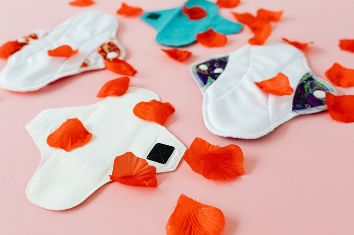 Four reusable cotton pads laid out on a pink surface and sprinkled with red petals