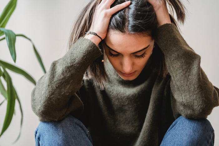 An anxious woman with eyes closed and clasping her hands in front of her face